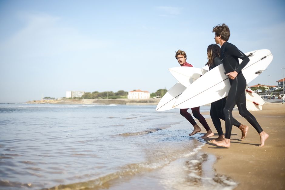 A group of friends in wetsuits with surfboards enjoying a sunny day on a Portuguese beach.