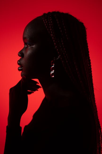 Silhouette of a woman with braided hair against a vivid red background, exuding bold and dramatic vibes.