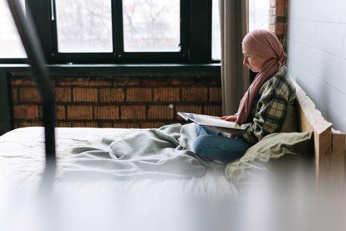 Free Woman in headwrap reading in a cozy brick-walled bedroom with natural light. Stock Photo
