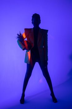 Artistic silhouette of a woman posing with a pineapple under vibrant lighting.