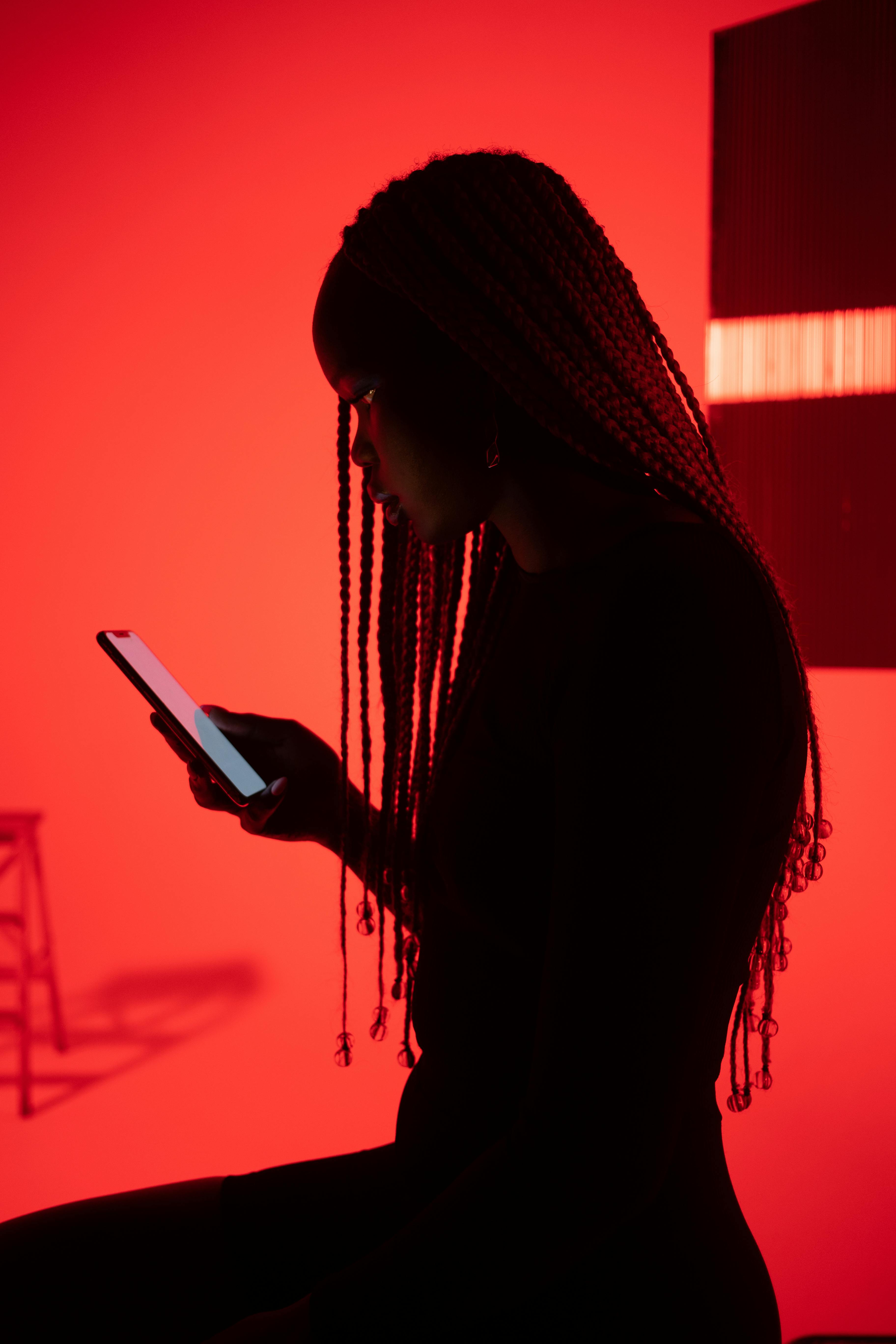 Silhouette of a woman using a smartphone against a vibrant red backdrop, emphasizing modern technology.