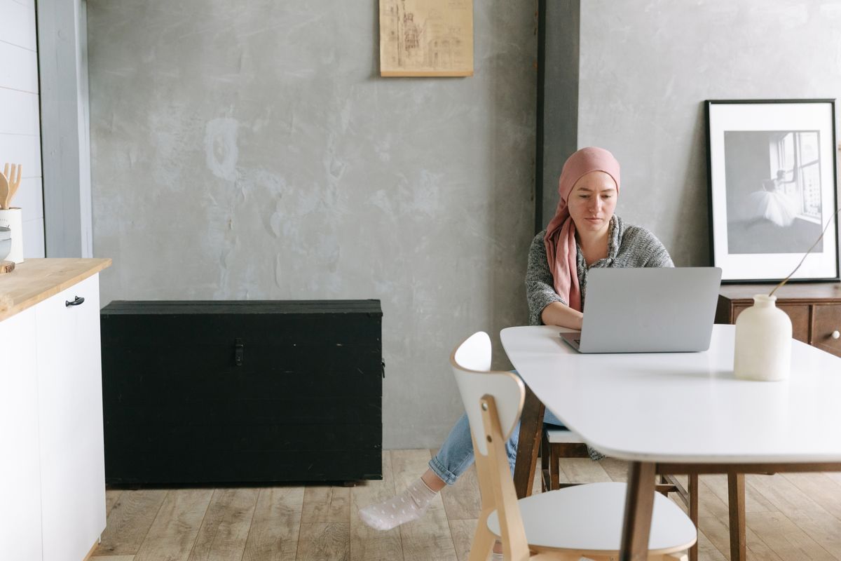 A woman wearing a headscarf uses a laptop in a modern, minimalist home interior.