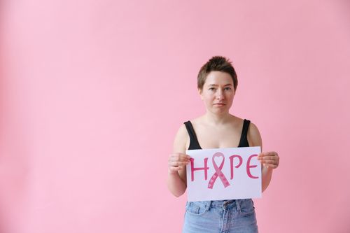 Free Woman holding a pink ribbon hope sign on pink background, symbolizing breast cancer awareness. Stock Photo