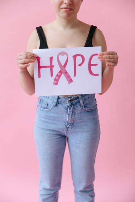 A woman in denim holds a hope sign for breast cancer awareness on a pink background.