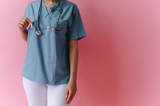 A medical professional holding a pink ribbon for breast cancer awareness against a pink background.