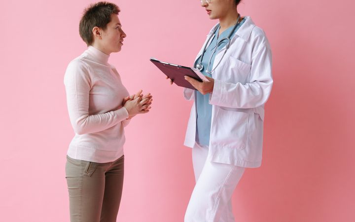 A medical professional consulting with a patient, against a pink background.