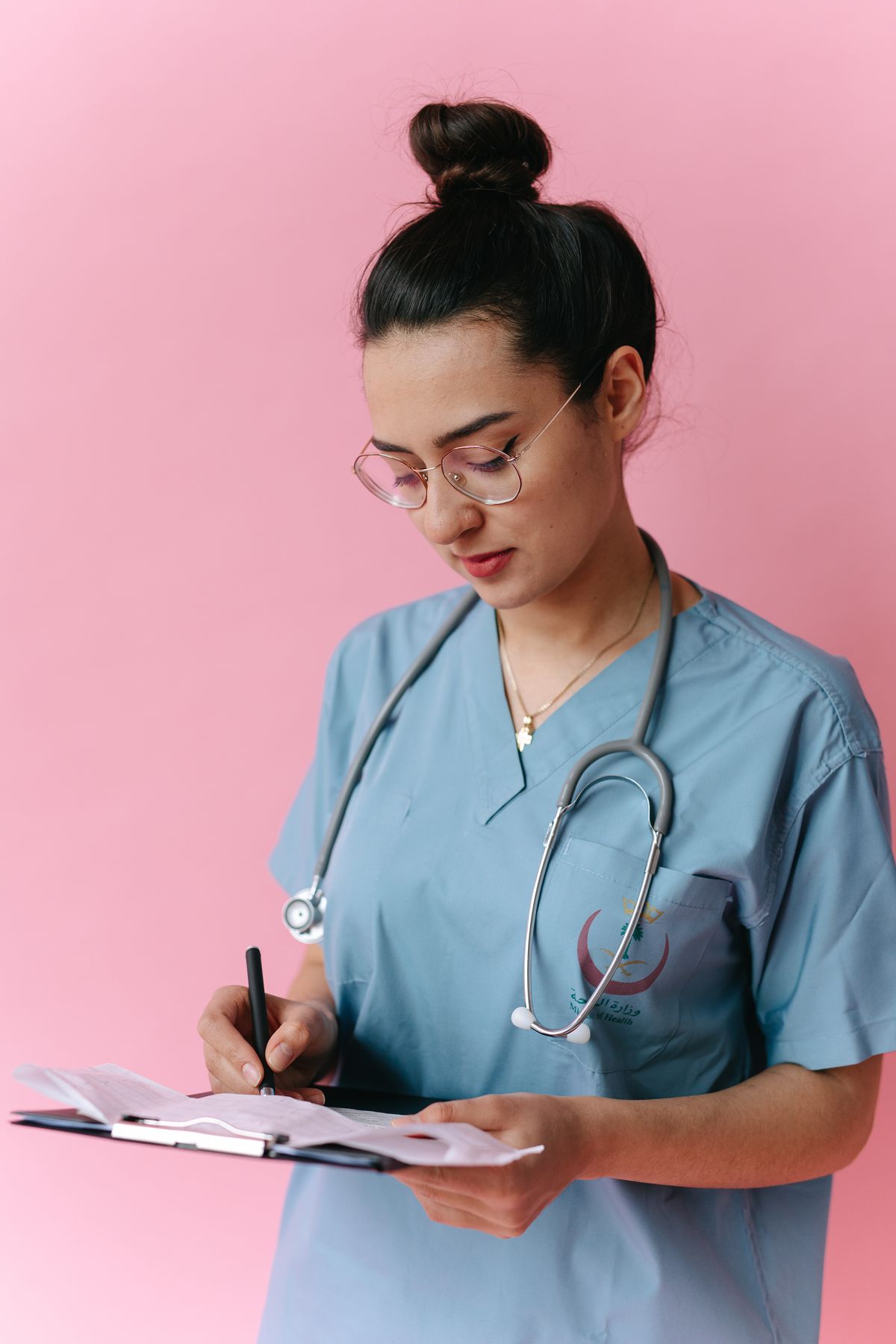 Nurse in scrubs writing notes on a clipboard