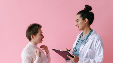 A doctor consults with a patient against a pink background, illustrating healthcare professionalism.