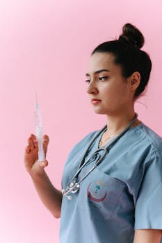A professional nurse in scrubs holding a syringe, set against a pink background.