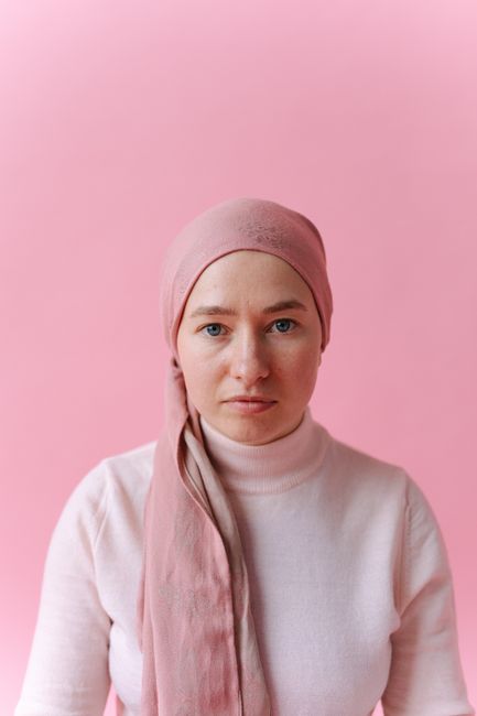 Close-up portrait of a woman wearing a pink headscarf against a pink background, conveying strength and hope.