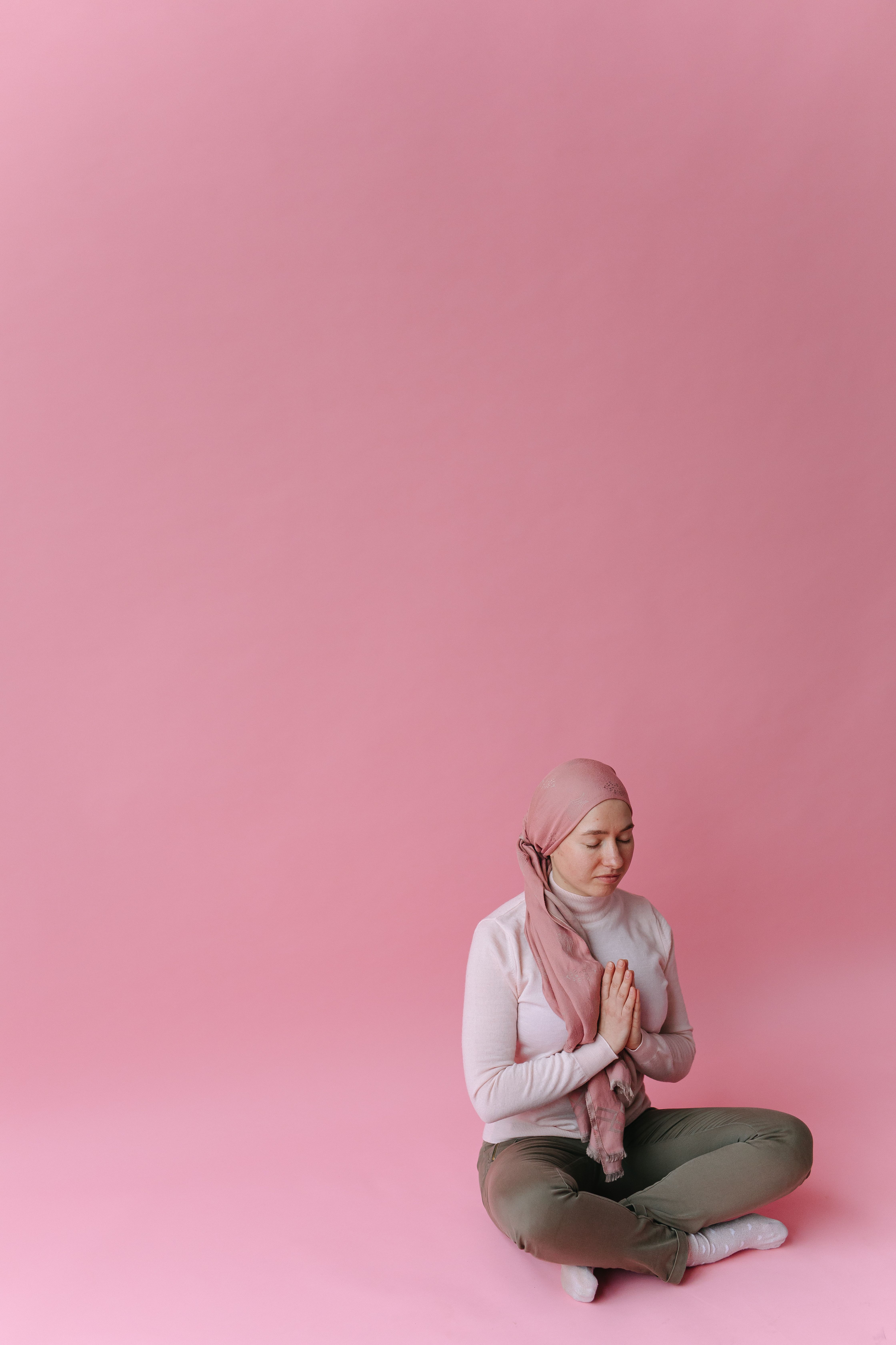 A woman in a headscarf meditating in a serene pink setting.