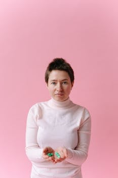 Woman with short hair holds pills in her hands, against a pink backdrop.
