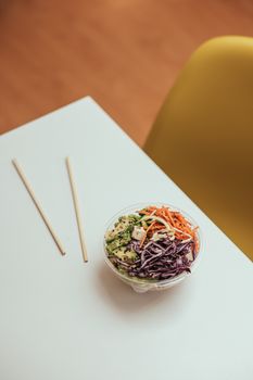 Top view of a vibrant vegetable salad in a bowl with chopsticks on a table, perfect for healthy dining.