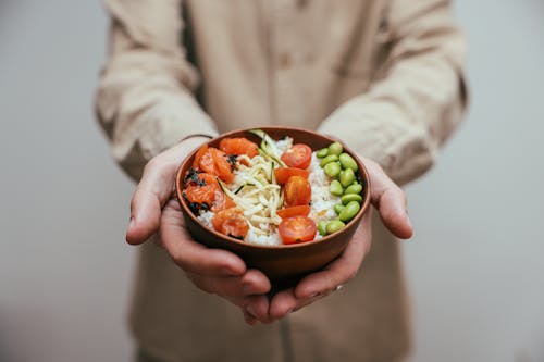 Person Holding a Rice Bowl with Vegetable Topping