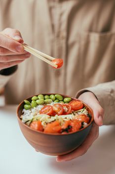 Close-up of hands holding a vibrant vegetable bowl with rice and edamame, perfect for a healthy meal.