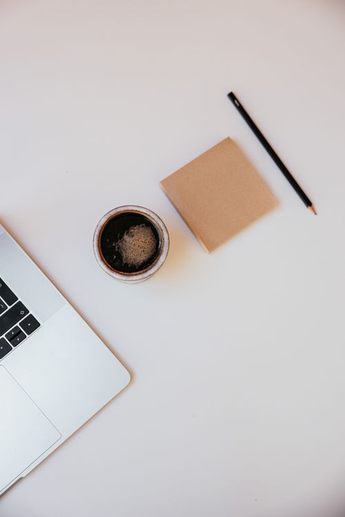 Free Stylish overhead view of a laptop, coffee cup, notepad, and pencil on a white desk. Stock Photo