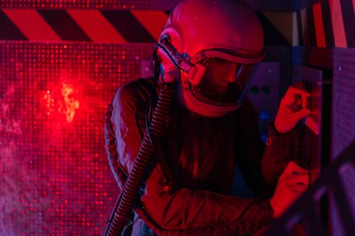Free A female astronaut operates a control panel under red lighting, evoking a sci-fi and futuristic atmosphere. Stock Photo