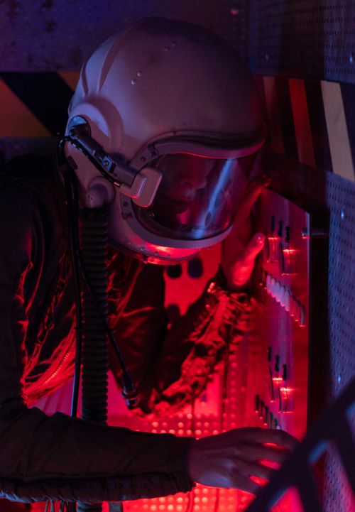 Free A female astronaut in a spacesuit operates a control panel with a red glow. Stock Photo