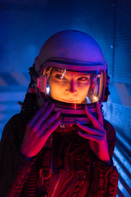 Free A woman cosmonaut in a space suit gazing sideways with vibrant lighting in a modern, sci-fi setting. Stock Photo