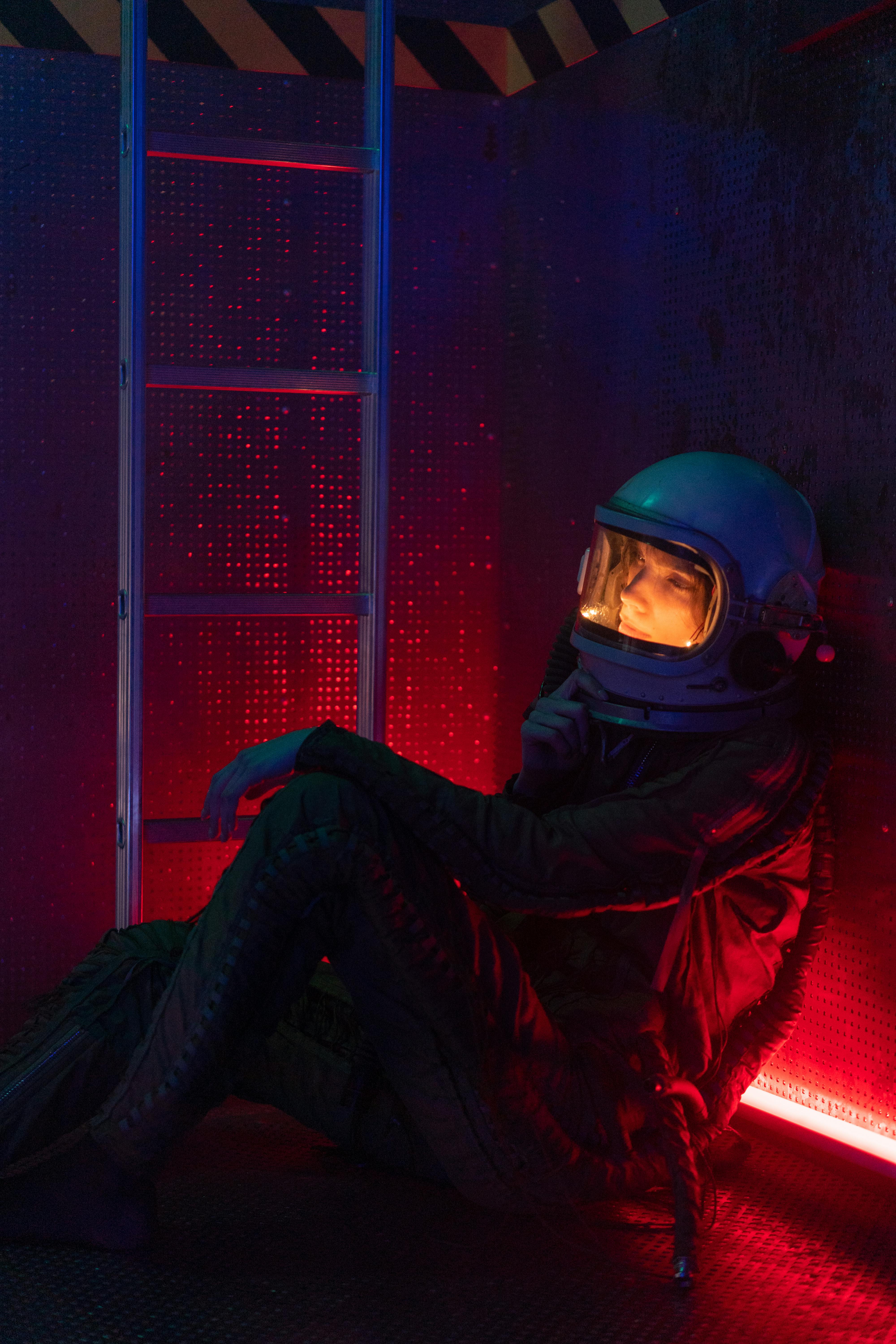 A contemplative astronaut in a dimly lit sci-fi setting, wearing a spacesuit and helmet.