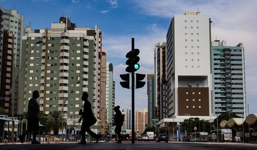 Free City scene with silhouettes walking across a street under towering buildings and a traffic light. Stock Photo