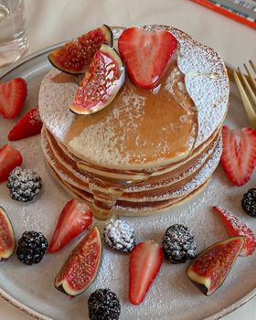 Stack of pancakes topped with figs, strawberries, and syrup, perfect for a sweet breakfast.