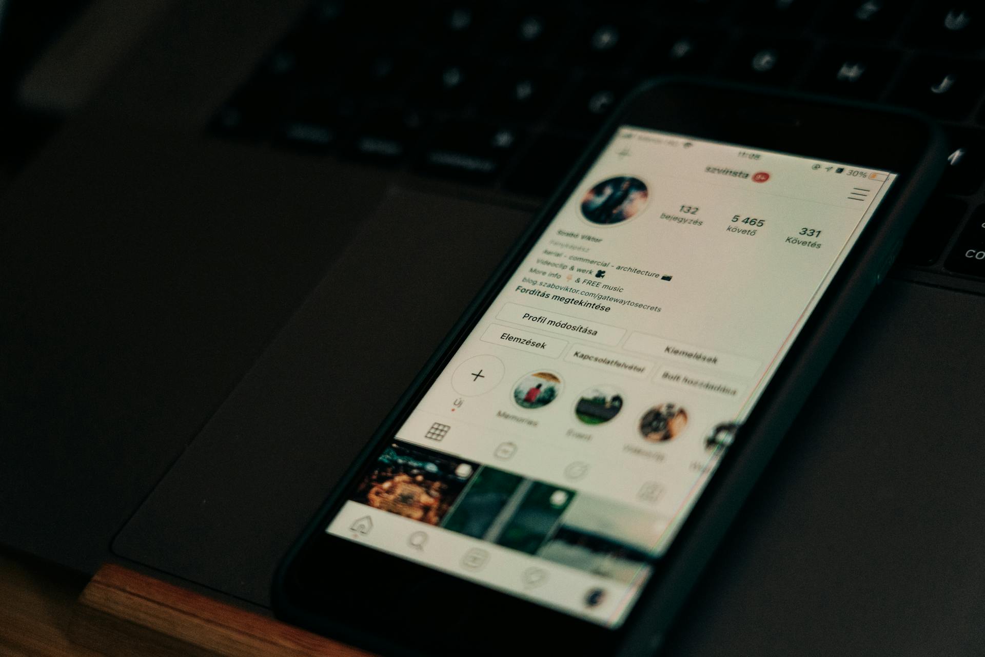 Close-up of smartphone showing a social media profile screen next to a laptop.