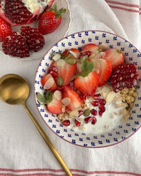 A vibrant breakfast bowl with strawberries, pomegranate, and granola on a cozy cloth backdrop.
