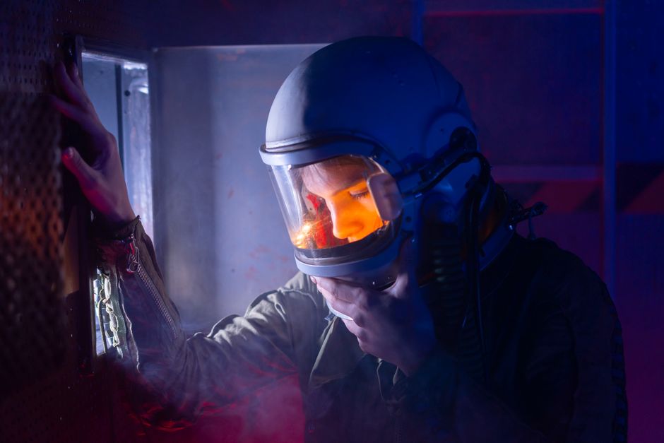 A contemplative astronaut in a helmet, illuminated by soft lighting, in a spacecraft setting.