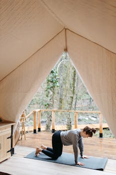 A woman practicing yoga inside a cozy tent with a scenic forest view outside.