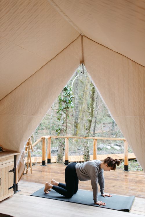 Free A woman practicing yoga inside a cozy tent with a scenic forest view outside. Stock Photo