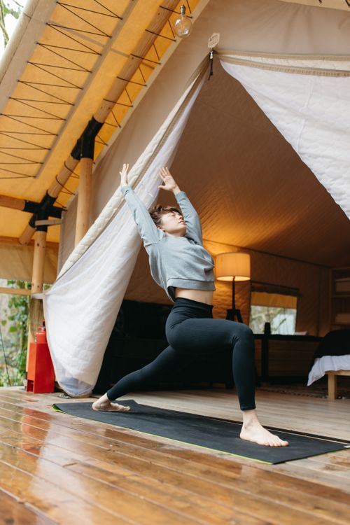 Free A woman performs a yoga pose in a serene outdoor tent setting, promoting relaxation and fitness. Stock Photo