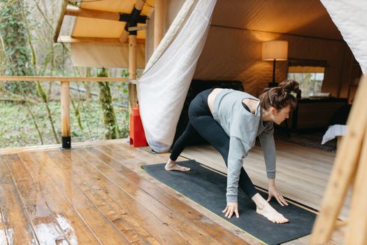 Woman stretching on a yoga mat at a glamping site, embracing nature and relaxation.