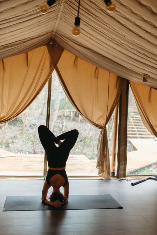 Free A woman performs a yoga headstand inside a sunlit tent, promoting calmness and flexibility. Stock Photo