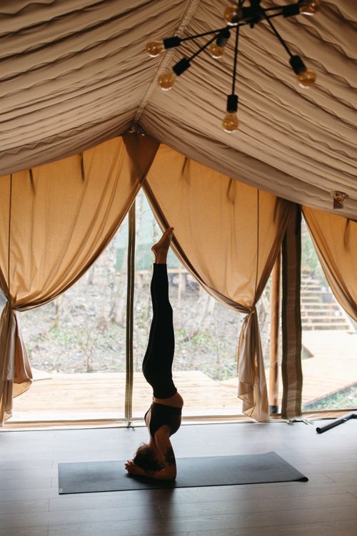 Free Woman practicing headstand yoga pose indoors with elegant curtains and natural light. Stock Photo