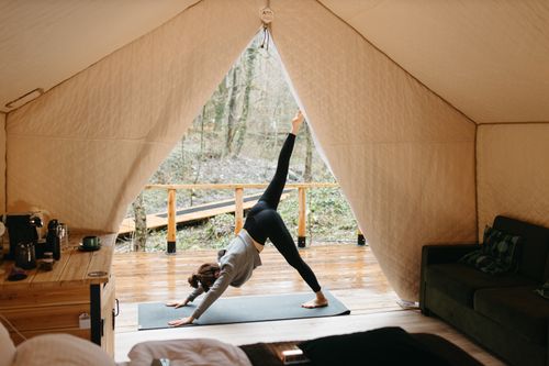 Free A woman performs yoga inside a glamping tent, surrounded by nature, embodying healthy living and relaxation. Stock Photo