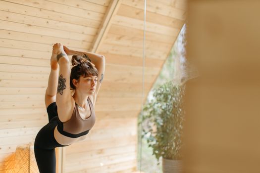 Woman doing a yoga pose in a wooden room, symbolizing health and relaxation.