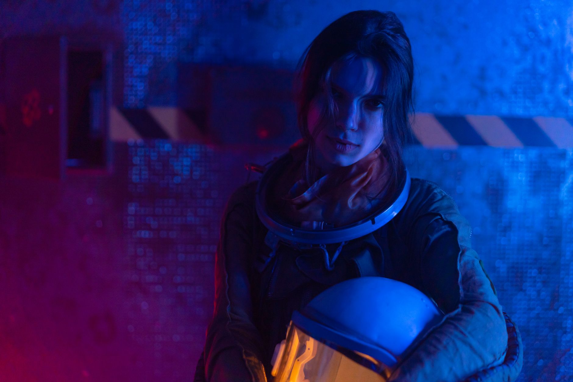 Portrait of a female astronaut with helmet under blue and red lights, exploring themes of space and technology.