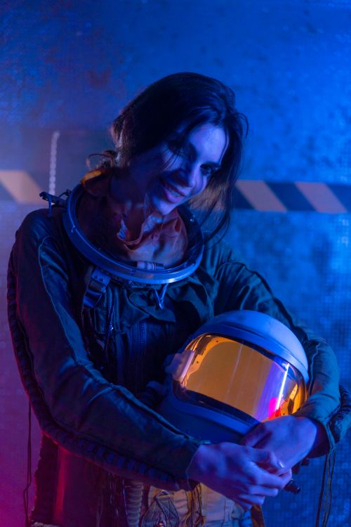 Free A woman in a spacesuit holding her helmet with a futuristic neon background, exuding a sci-fi theme. Stock Photo