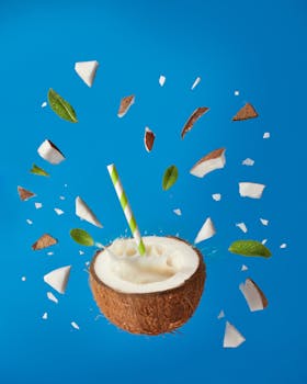 Dynamic image of a coconut drink with pieces and leaves against blue background, evoking tropical freshness.