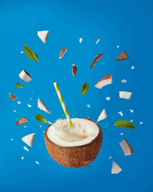 Free Dynamic image of a coconut drink with pieces and leaves against blue background, evoking tropical freshness. Stock Photo