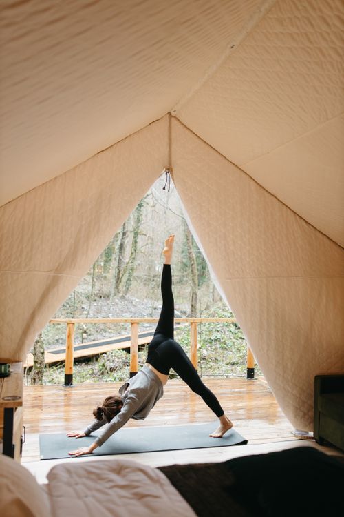 Free Woman performing yoga inside a cozy glamping tent surrounded by nature. Stock Photo