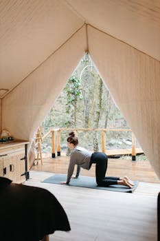 A woman performing yoga poses inside a glamping tent in a serene forest setting, focusing on wellness and relaxation.