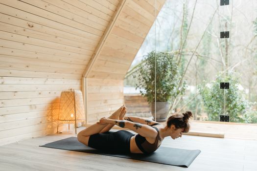 Woman practicing yoga in a serene, light-filled wooden cabin, focusing on health and wellbeing.