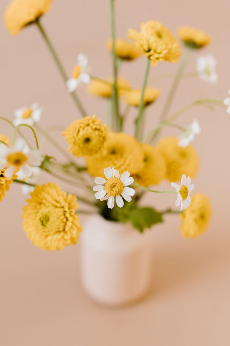 Bright yellow and white flowers in a vase against a neutral background, perfect for decor themes.