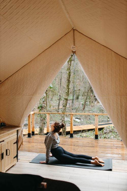 Free A woman stretches in a tent, practicing yoga on a mat in an outdoor forest setting. Stock Photo