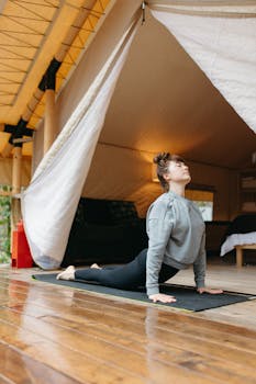 A woman practicing yoga on a mat within a cozy glamping tent with wooden floors.