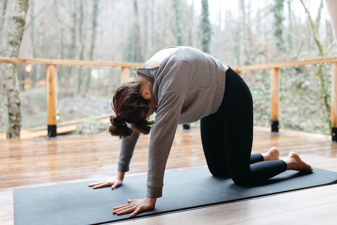 Woman in Gray Long Sleeve Shirt and Black Leggings Doing Yoga on Black Yoga Mat