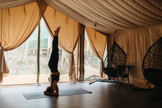 A woman performs a headstand yoga pose inside a cozy glamping tent with natural light.