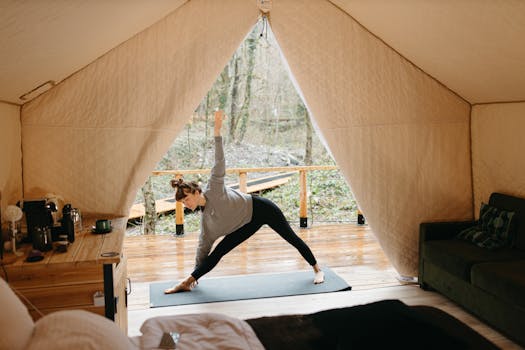 A woman performs a yoga pose on a mat inside a cozy tent with a woodland view.